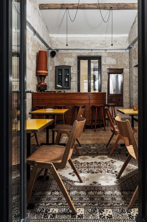 Salle à manger de l'Hôtel La Prison à Béziers avec chaises en bois années 50, tables jaunes et murs en pierre apparente