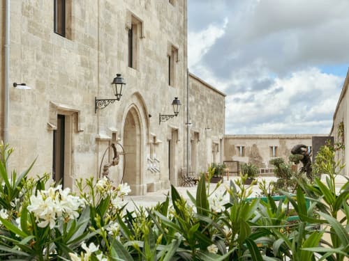 Patio histórico de piedra en Hotel La Prison Béziers con flores blancas, arco de entrada y faroles tradicionales