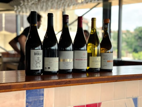 Botellas de vino exhibidas en el mostrador de bar de madera del Hotel La Prison en Béziers, Francia