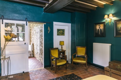 Chambre Bougros au Prieuré Du Preux : murs bleu-vert, fauteuils jaunes, poutres apparentes, vue sur le jardin