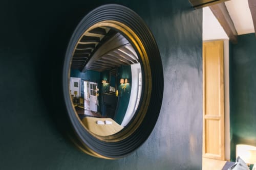 Miroir convexe reflétant le couloir de l'hôtel-boutique Le Prieuré Du Preux aux murs vert forêt et détails dorés
