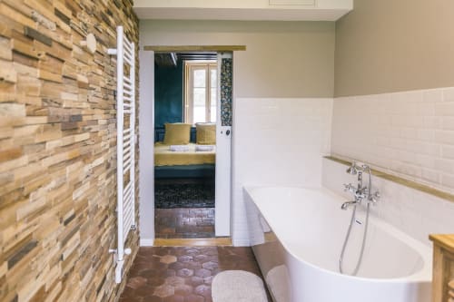 Salle de bains de la chambre Bougros au Prieuré Du Preux avec baignoire îlot, mur de briques et accès à la chambre avec jardin