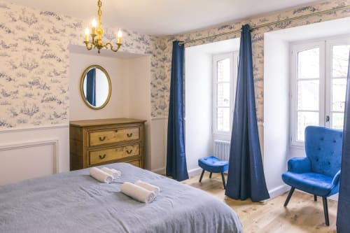 Blanchot room at Le Prieuré Du Preux with toile wallpaper, blue armchair, wooden dresser, and garden view windows