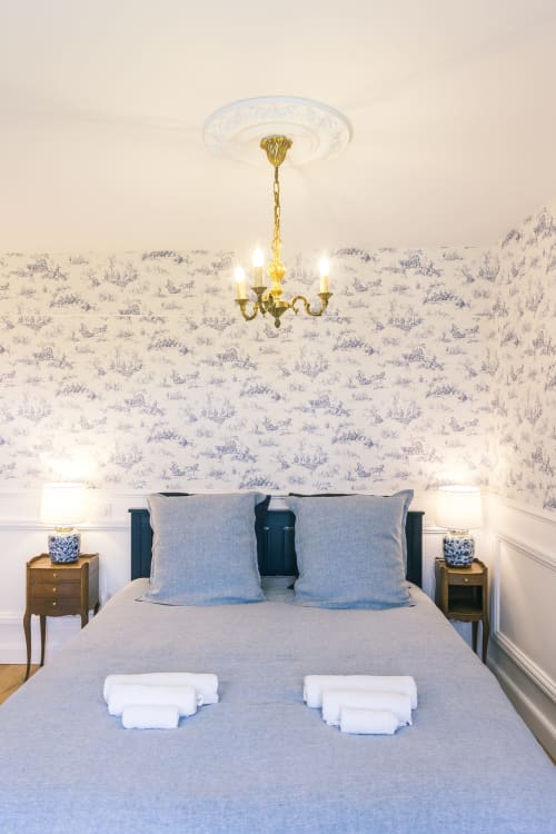 Chambre élégante du Prieuré du Preux avec papier peint bleu toile, lustre en laiton et vue sur le jardin à Sépeaux Saint Romain