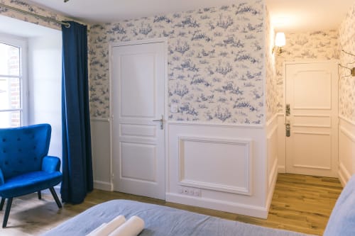 Élégante chambre du Prieuré Du Preux avec papier peint bleu toile, fauteuil velours bleu, armoire blanche et parquet
