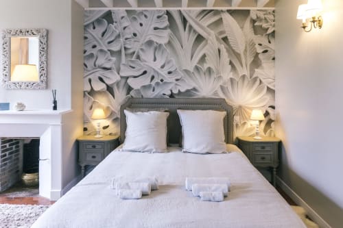 Valmur room at Le Prieuré Du Preux with white bed, ornate headboard, botanical wall art, and fireplace