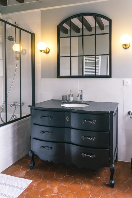 Modern black vanity with round sink and arched mirror in Valmur room at Le Prieuré Du Preux, France