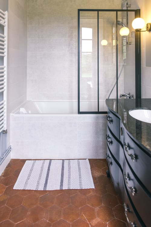 Modern bathroom with bathtub, black-framed shower enclosure, dark vanity, and terracotta tile floor at Le Prieuré Du Preux