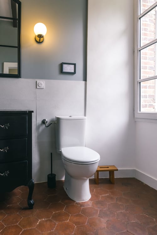 Modern bathroom in Valmur room at Le Prieuré Du Preux with white toilet, hexagon tiles, and brass wall sconce lighting