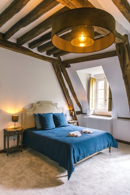 Cozy attic bedroom at Le Prieuré Du Preux with blue bedding, wooden beams, and garden view