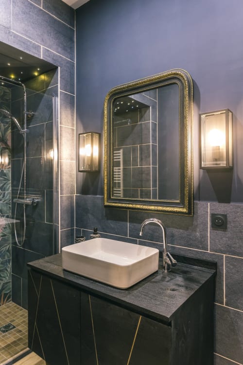 Salle de bains moderne aux murs en carrelage foncé, vasque blanche, miroir doré et douche à effet pluie de la chambre VAUDESIR au Prieuré