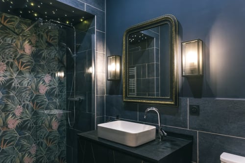 Salle de bains moderne au Le Prieuré Du Preux avec murs en carrelage noir, vasque blanche et miroir orné cadre doré