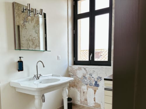 Lavabo rústico del Hotel La Prison con lavamanos de pedestal, espejo y ventana de marco negro con vistas a Béziers