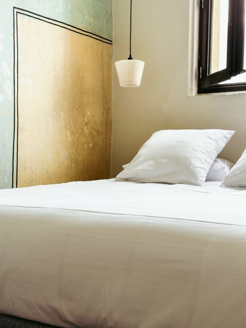 Habitación moderna del hotel La Prison en Béziers con ropa de cama blanca, pared acentuada en dorado, luz colgante y ventana con marcos negros