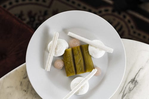 Plato artístico del Hotel La Prison con hojas de plátano, espuma blanca y microbrotes sobre mesa de mármol en Béziers