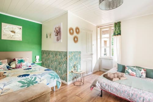 Helles Schlafzimmer im La Maison de la Colline mit grüner Akzentwand, tropischer Bettwäsche und Gartenblick in Vers, Frankreich