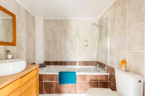 Modernes Badezimmer in La Maison de la Colline in Vers, Frankreich mit Badewanne, Holzwaschbecken und braunen Fliesenakzenten