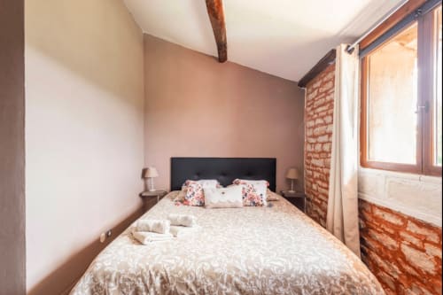 Gemütliches Schlafzimmer in La Maison de la Colline mit sichtbarem Mauerwerk, Holzbalken, schwarzem Kopfteil und Gartenblick in Vers