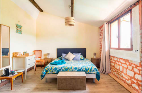 Helles Schlafzimmer in La Maison de la Colline in Vers, Frankreich mit blauem Gemusterbett, sichtbarem Ziegelwerk und Garten