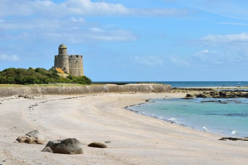 Historic stone tower on sandy beach at RELAIS DES ILES, Saint Marcouf, France with turquoise waters
