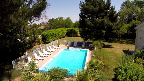 Swimmingpool mit Liegen im Le Manoir Lacustre in Queyrac, umgeben von üppigen Gärten und Bäumen