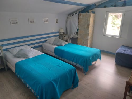 Helles Schlafzimmer im Le Manoir Lacustre in Queyrac mit zwei Einzelbetten, blauer Bettwäsche und Gartenfensterblick