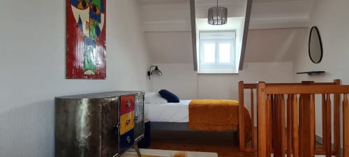 Cozy bedroom at Relais des Iles cottage with wooden bed, metal trunk, colorful artwork, and sea-view window in Saint-Marcouf