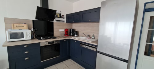 Modern kitchen with dark blue cabinetry, wood countertops, and stainless steel appliances at Relais des Iles cottage,