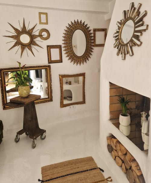 Entrée de villa éclectique avec miroirs soleil dorés et cadres décoratifs sur murs blancs, étagère en bois avec plante et tissé