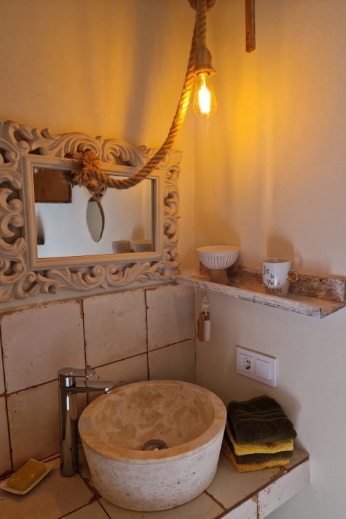 Salle de bains rustique avec lavabo en pierre, miroir orné et luminaire suspendu en corde à la villa Las Fincas De Annie à Felanitx