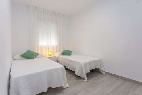 Dormitorio doble con almohadas verdes, ropa de cama blanca y linterna amarilla en el apartamento Wehost Costaluz de Puerto Santa María