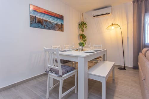 Comedor moderno en apartamento Las Dunas de Wehost Costaluz Puerto Santa María con mesa blanca, sillas y asientos de banco