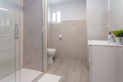 Baño moderno en apartamento Wehost Costaluz en Puerto Santa María con ducha azulejos, inodoro, lavamanos y piso efecto madera