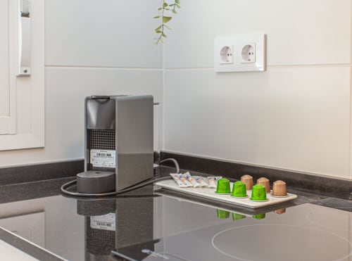 Moderna encimera de cocina con máquina de espresso, cápsulas de café verde y enchufes blancos en apartamento de Puerto Santa María