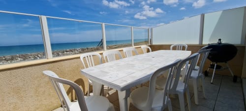 Beachfront terrace at RELAIS DES ILES cottage with dining table, white chairs, barbecue, and sea views in Saint-Marcouf