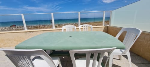 Terrasse de restauration en bord de mer au Relais des Îles avec table verte et chaises blanches donnant sur la plage de sable et la mer bleue