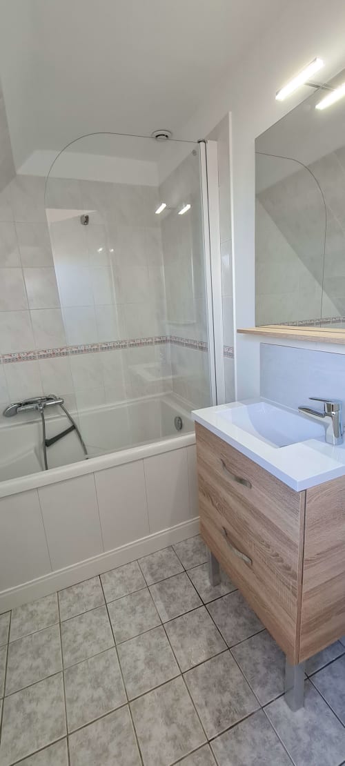 Modern bathroom with glass shower enclosure, wooden vanity with white sink, and bright LED lighting at Relais des Iles