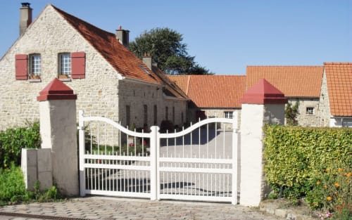 White gate entrance to Domaine De La Ronville stone cottage with terracotta roof in France