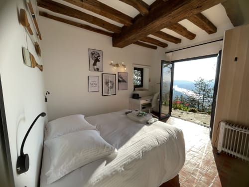 Chambre lumineuse aux poutres apparentes, lit blanc et portes ouvertes sur les montagnes au Paradis de Lucile, La Roche Guyon.