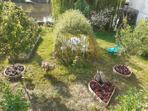 Jardin du refuge des Alpes mancelles avec fleurs plantées, plantes en pot et vue sur l'eau à Fresnay-sur-Sarthe