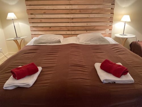 Geräumiges Schlafzimmer im La Croix De La Jarrie BnB in Châtres mit Holzkopfteil, braunem Bettüberwurf, weißen Kissen und rotem Rollstoff