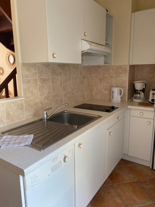 Kompakte ausgestattete Küche mit weißen Schränken, beigefarbener Fliesenrückwand und Edelstahlspüle im Duplex La Croix De La Jarrie