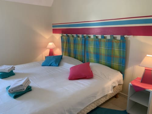 Farbenfrohe Schlafzimmer in der Gästepension La Croix De La Jarrie, Châtres, mit blauem Karostoffkopfteil, roten Akzenten und weißer Bettwäsche