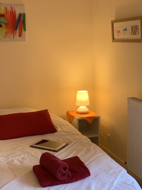 Gemütliches Schlafzimmer in La Croix De La Jarrie mit leuchtender Lampe, rotem Kissen, Tablet auf dem Bett und gerahmtem Kunstwerk in Châtres