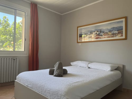 Bright bedroom at La Conciergerie De Franck villa in Boissieres with white bed, garden view window, and Tuscan landscape