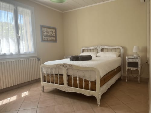 Bright bedroom with white ornate bed frame, cream bedding, and garden view at La Conciergerie De Franck villa in Boissieres