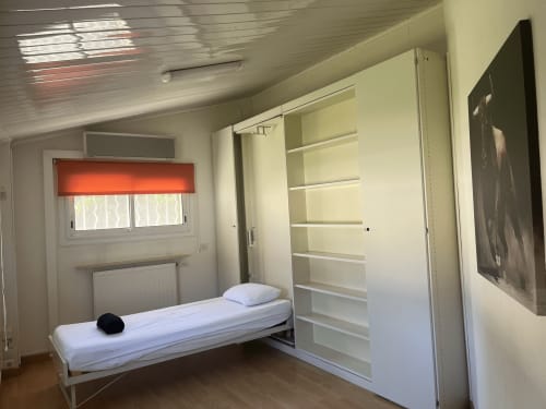 Bright modern bedroom at La Conciergerie De Franck villa with single bed, built-in shelving, and garden view window with