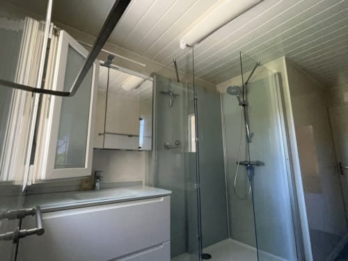 Modern bathroom with white vanity, mirror, and walk-in shower with glass enclosure at La Conciergerie De Franck villa