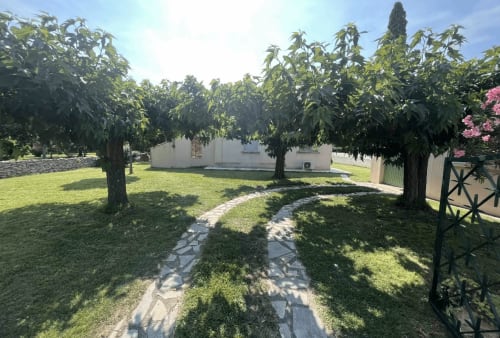 Shaded garden pathway at La Conciergerie De Franck villa in Boissieres, France with mature trees and white building.