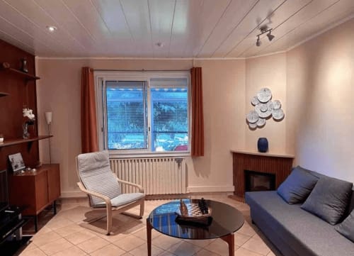 Modern villa sitting area at La Conciergerie De Franck with blue sofa, lounge chair, fireplace and garden view
